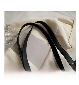 Detail of white quilted tote bag featuring black leather handles and gold metal buckles