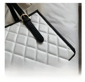 Detail view of white quilted tote bag featuring black leather trim and gold metal hardware