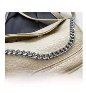 Detalle de cuero crema granulado y cadena metálica plateada en el bolso de hombro