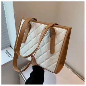 Detail of white quilted tote bag featuring brown leather trim and gold metal buckles