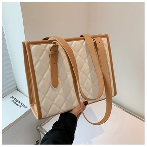 Detail of white quilted tote bag with brown leather straps and adjustable metal buckle