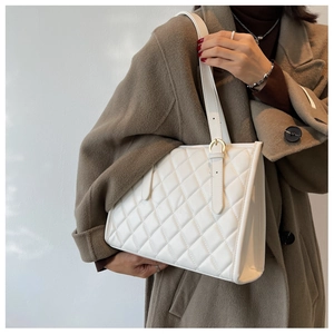 Detail of ivory quilted tote bag with adjustable strap worn over a brown wool coat