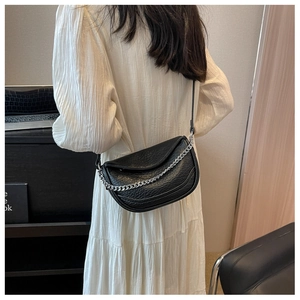 Detalle de bolso montura negro con textura granulada y cadena plateada en vestido blanco