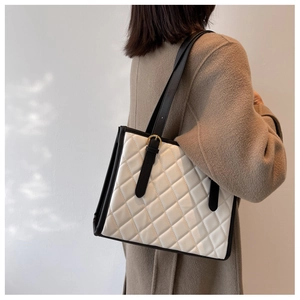 Close-up of beige quilted tote bag with black straps worn on a model shoulder