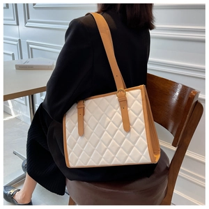 Detail of white quilted tote bag with brown leather trim and adjustable gold buckle