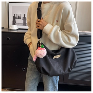 Detail of black nylon crescent crossbody bag with fashion label and peach plush charm