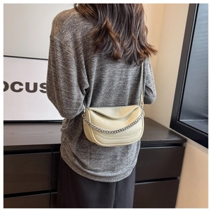 Bolso de montura beige en cuero texturizado con cadena plateada visto de lado en modelo