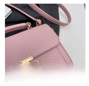 Gros plan d'un sac rose avec texture cuir grainé et fermoir rotatif en métal doré
