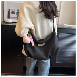 Detail of black nylon pleated crossbody bag with leather tag and peach plush pendant