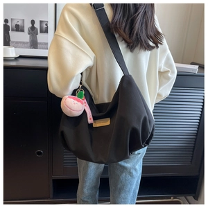 Close-up of black nylon dumpling bag featuring brown leather patch and pink plush charm