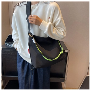 Detail of black nylon crossbody bag with fluorescent green zipper pull and red side label
