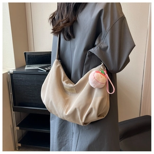 Detail view of beige nylon dumpling bag with peach plush charm and side strap design