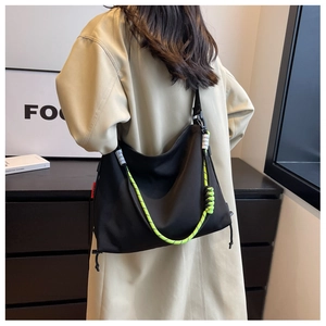 Detail of large black nylon tote featuring neon green braided rope strap and side red label