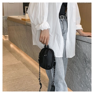 Detail of black nylon mini crossbody bag with woven strap shown on white shirt outfit