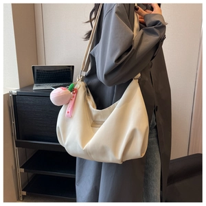 Close-up of a cream nylon dumpling bag with pleated design and a peach plush charm