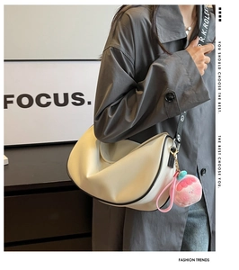 Detail of cream crescent bag with wide logo strap and pink plush charm accessory
