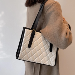 Quilted tote bag with black straps and gold buckles worn over a classic tan wool coat