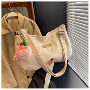 Close-up of beige nylon crossbody bag featuring leather logo tag and pink peach plush charm