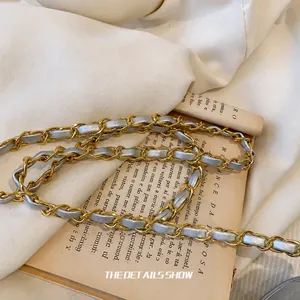 Détail macro d'une bandoulière en chaîne dorée entrelacée de cuir gris argenté chic
