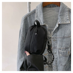 Detail view of a black nylon crossbody bag with striped strap on a denim jacket model