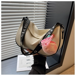 Detail of cream half-moon saddle bag with wide lettered strap and peach plush charm