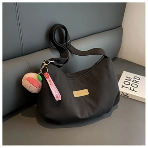 Detail of black nylon crescent bag with adjustable strap and peach plush pendant