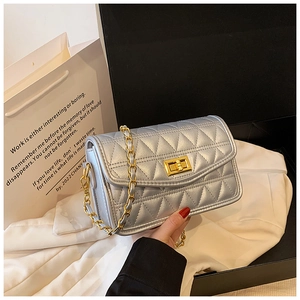 Détail d'un sac matelassé argenté avec fermoir doré et sa chaîne dans un coffret cadeau