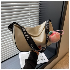 Detail of cream saddle bag featuring a wide logo strap and a cute pink peach charm