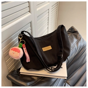 Detail of black nylon dumpling bag featuring a brown leather patch and cute pink doll charm