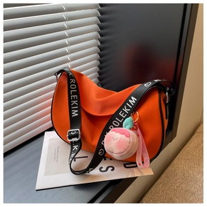 Detail of orange saddle bag featuring branded wide strap and pink peach pendant