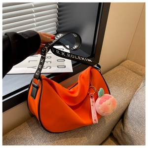 Detail of bright orange crescent bag featuring wide letter strap and peach charm