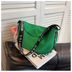 Detail of green crescent saddle bag with logo strap and pink peach charm on books