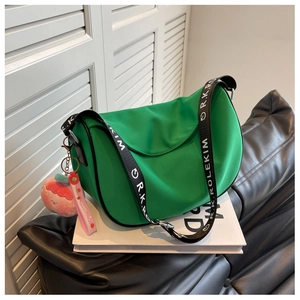 Detail of green crescent saddle bag with wide branded strap and peach plush charm