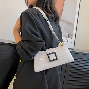 Minimalistische witte okseltas met krokodillenpatroon en gedraaide riem gedragen door model