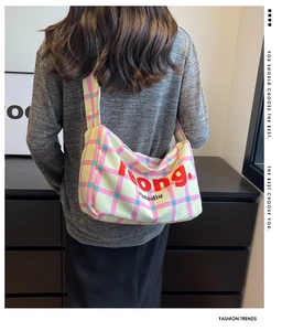 Model wearing a colorful plaid canvas crossbody bag with wide shoulder strap and text detail