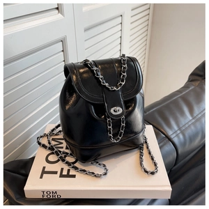Detail of a black glossy mini backpack with silver twist lock and chain strap on a white book