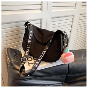 Detail of black crescent crossbody bag featuring wide lettered strap and peach plush charm