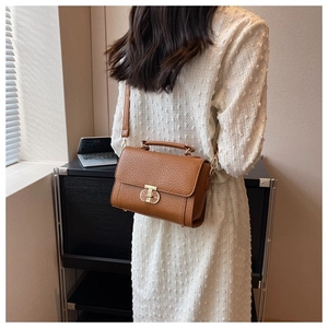Détail d'un petit sac carré en cuir marron avec fermoir doré sur une robe blanche
