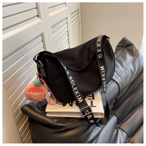 Close-up of black crescent saddle bag with wide logo strap and pink peach charm