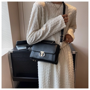 Détail du sac bandoulière noir en cuir texturé avec fermoir doré sur robe blanche