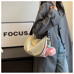 Detail of a beige hobo bag with black contrast trim and a pink plush donut charm