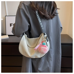 Side view of ivory hobo bag with wide logo strap and pink plush charm accessory