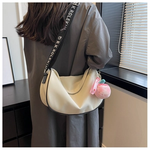 Detail of cream crescent shoulder bag featuring a branded wide woven strap and pink plush charm