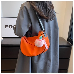 Detail of orange crescent bag with wide logo strap and pink plush charm accessory