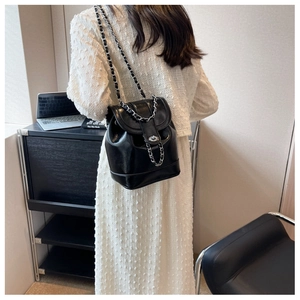 Detail of glossy black leather backpack with silver twist lock and chain strap design