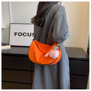 Vibrant orange crescent shoulder bag with wide jacquard strap and peach plush charm detail