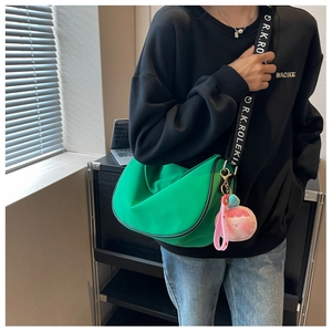 Detail of green crescent saddle bag with wide logo strap and pink plush pendant