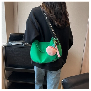 Detail of green hobo bag with adjustable lettered strap and peach plush pendant