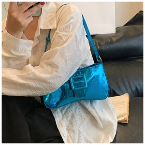 Detail of blue crocodile pattern underarm bag with oversized decorative buckle strap