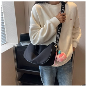 Close-up of black crescent saddle bag with wide branded strap and peach charm